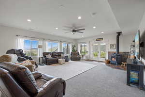 Carpeted living room with ceiling fan, french doors, and a wood stove