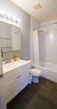 Full bathroom with wood-type flooring, shower / bath combo with shower curtain, a textured ceiling, vanity, and toilet