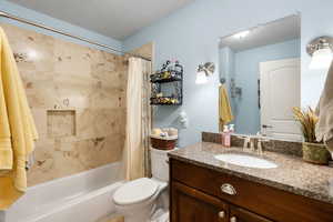 Full bathroom featuring a textured ceiling, toilet, vanity, and shower / bathtub combination with curtain