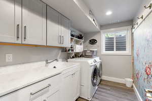 Laundry area featuring sink, washing machine and dryer, light wood-type flooring, and cabinets