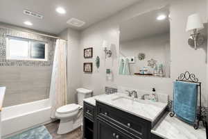 Full bathroom with wood-type flooring, toilet, shower / tub combo with curtain, and vanity