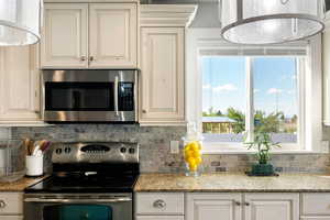 Kitchen with decorative backsplash, appliances with stainless steel finishes, and light stone counters