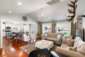 Living room featuring a textured ceiling, an inviting chandelier, dark hardwood / wood-style floors, and lofted ceiling