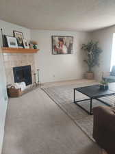 Carpeted living room featuring a tiled fireplace and a textured ceiling