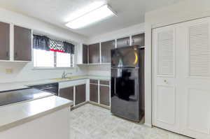 Kitchen featuring sink, black appliances, light tile patterned floors.