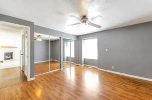 Unfurnished master bedroom featuring a tile fireplace, wood-type flooring, multiple closets, a textured ceiling, and ceiling fan.