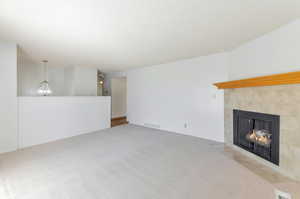 Unfurnished living room with a notable chandelier, a tile fireplace, a textured ceiling, and carpet flooring.