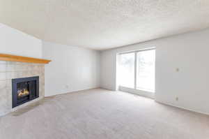 Unfurnished living room with carpet, a textured ceiling, and a tile fireplace.