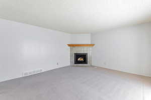 Unfurnished living room featuring a textured ceiling, carpet, and a tile fireplace.