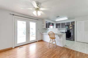 Kitchen featuring ceiling fan, light wood-type flooring, a kitchen bar, kitchen peninsula, and black refrigerator.