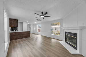 Unfurnished living room featuring light hardwood / wood-style floors, ceiling fan, a tile fireplace, and a textured ceiling