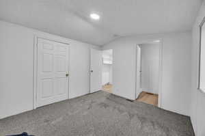 Unfurnished bedroom featuring a closet, vaulted ceiling, connected bathroom, and light colored carpet