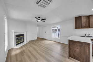 Unfurnished living room with ceiling fan, light hardwood / wood-style flooring, sink, a fireplace, and a textured ceiling