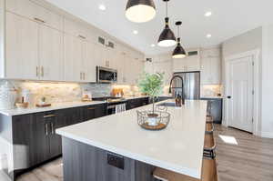 Kitchen featuring appliances with stainless steel finishes, an island with sink, a kitchen bar, decorative backsplash, and light wood-type flooring