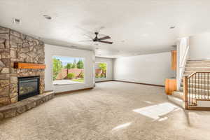 Unfurnished living room with ceiling fan, a textured ceiling, light carpet, and a fireplace