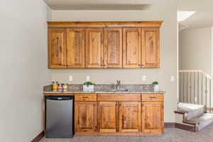 Kitchen with stainless steel dishwasher, sink, light stone counters, and light carpet