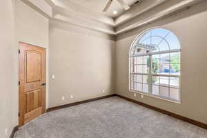 Carpeted empty room with ceiling fan and a tray ceiling