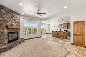 Living room with ceiling fan, a textured ceiling, light tile patterned floors, and a stone fireplace