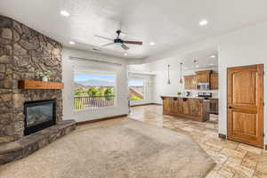 Carpeted living room featuring ceiling fan, a fireplace, and a textured ceiling