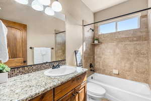 Full bathroom with tasteful backsplash, vanity, tiled shower / bath combo, and toilet