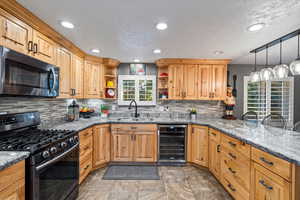 Kitchen with decorative backsplash, sink, black appliances, light tile patterned floors, and beverage cooler