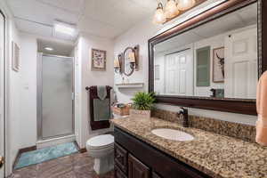 Bathroom featuring a paneled ceiling, tile patterned floors, vanity, toilet, and walk in shower