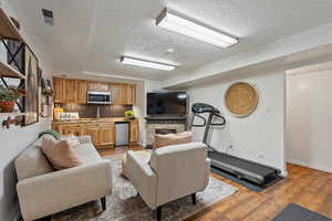 Living room with sink, a textured ceiling, light hardwood / wood-style flooring, and a stone fireplace