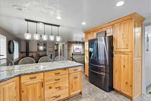 Kitchen featuring hanging light fixtures, light stone counters, light tile patterned floors, stainless steel fridge with ice dispenser, and a textured ceiling