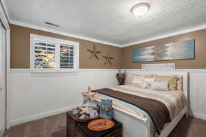 Bedroom with a textured ceiling, carpet floors, and ornamental molding