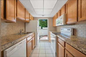 Kitchen featuring sink, decorative backsplash, white appliances, and light tile patterned floors