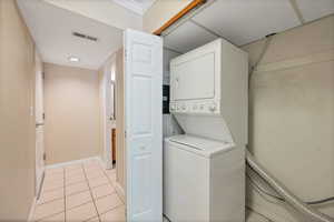 Clothes washing area featuring light tile patterned flooring and stacked washing maching and dryer