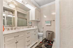 Bathroom featuring crown molding, tile patterned floors, tile walls, toilet, and dual vanity