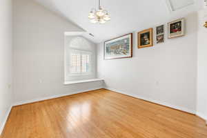 Spare room with an inviting chandelier, light wood-type flooring, and vaulted ceiling