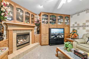 Living room with ceiling fan, a textured ceiling, a tiled fireplace, and tile walls