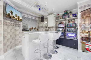 Kitchen featuring light stone countertops, white cabinetry, tile walls, ornamental molding, and a breakfast bar