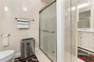 Bathroom with a shower with door, toilet, tile patterned flooring, vanity, and tile walls