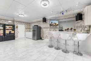 Kitchen featuring stainless steel fridge, wall chimney exhaust hood, tile walls, white cabinets, and ornamental molding