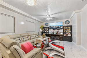 Living room with ceiling fan with notable chandelier, light tile patterned flooring, and ornamental molding