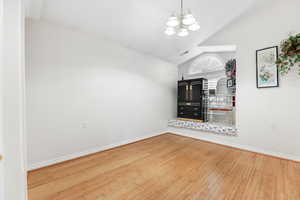 Spare room featuring hardwood / wood-style flooring, a chandelier, and vaulted ceiling