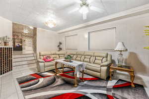 Tiled living room featuring ceiling fan, tile walls, and crown molding