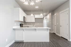 Kitchen featuring appliances with stainless steel finishes, hanging light fixtures, a kitchen breakfast bar, sink, and white cabinetry