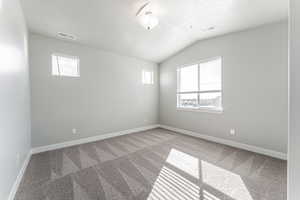 Carpeted empty room with a textured ceiling and vaulted ceiling