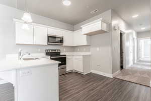 Kitchen featuring kitchen peninsula, stainless steel appliances, decorative light fixtures, sink, and white cabinets