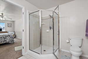 Bathroom featuring ceiling fan, tile patterned flooring, a shower with door, and toilet