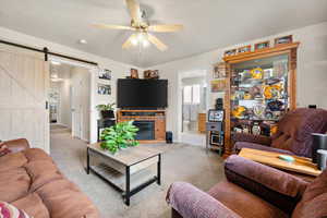 Living room with ceiling fan, a barn door, and light carpet