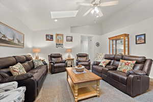 Carpeted living room with ceiling fan and lofted ceiling with skylight