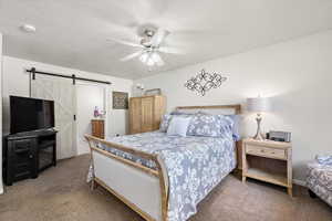 Bedroom featuring ceiling fan, connected bathroom, dark carpet, and a barn door