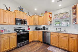 Kitchen with stainless steel appliances, vaulted ceiling, dark wood-type flooring, and tasteful backsplash