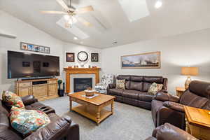 Living room featuring light colored carpet, lofted ceiling with skylight, and ceiling fan