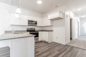 Kitchen with appliances with stainless steel finishes, decorative light fixtures, sink, white cabinetry, and kitchen peninsula